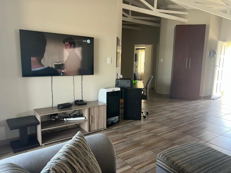 A living area featuring tiled flooring and exposed roof trusses, with a built-in cupboard and neutral wall finishes.