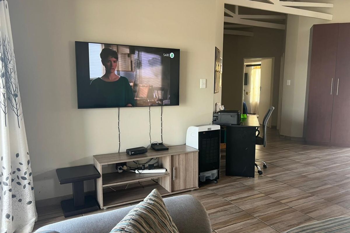 A living area featuring tiled flooring and exposed roof trusses, with a wall-mounted television and adjacent built-in storage cabinetry.