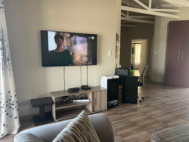 A living area featuring tiled flooring and exposed roof trusses, with a wall-mounted television and adjacent built-in storage cabinetry.