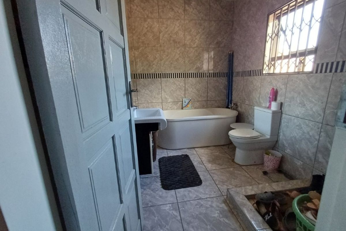 A functional bathroom featuring a bathtub, pedestal basin, and toilet, finished with neutral wall and floor tiling.