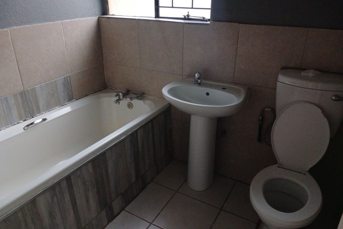 A functional bathroom featuring a standard bathtub, pedestal basin, and toilet with neutral wall and floor tiling.