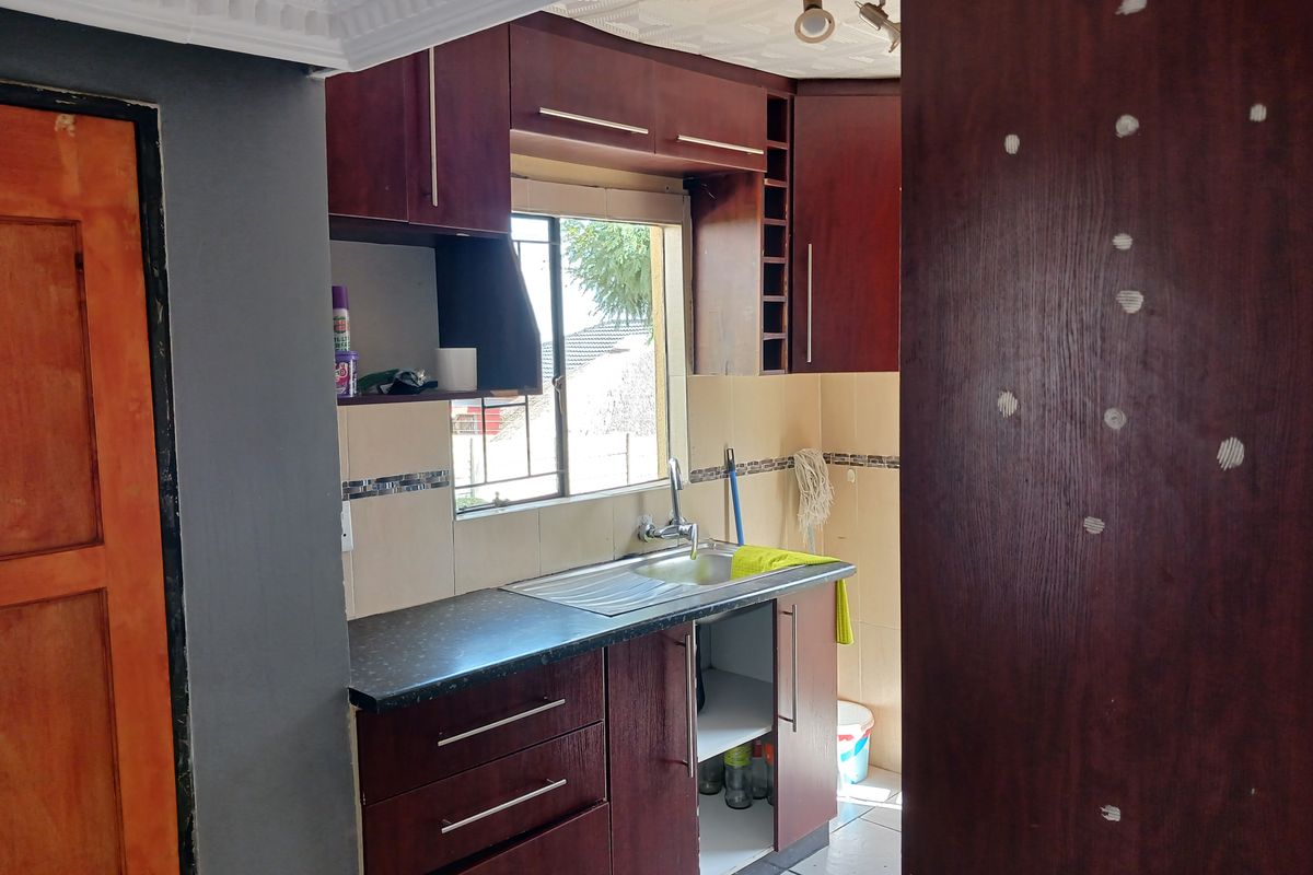 A compact kitchen featuring dark wood cabinetry, a stainless steel sink, tiled backsplash, and a window providing natural light.