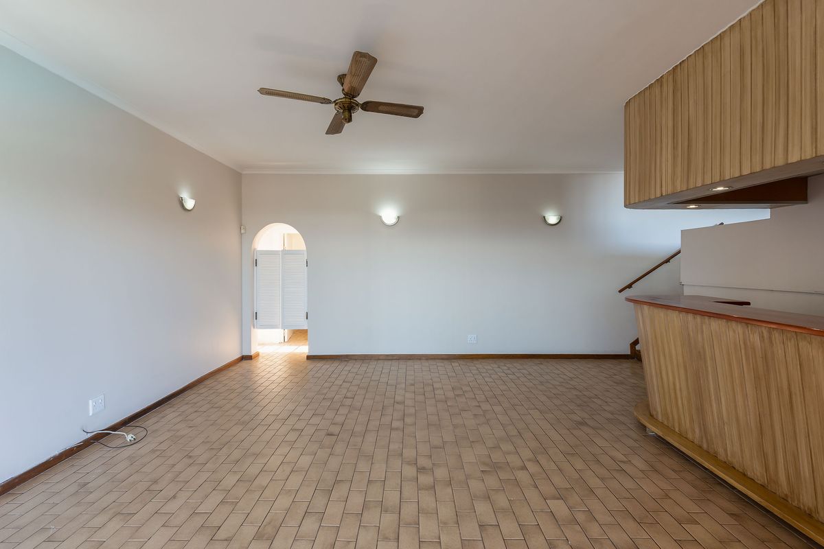 Spacious living area featuring tiled flooring, a built-in bar, ceiling fan, and an arched doorway leading to adjacent spaces.