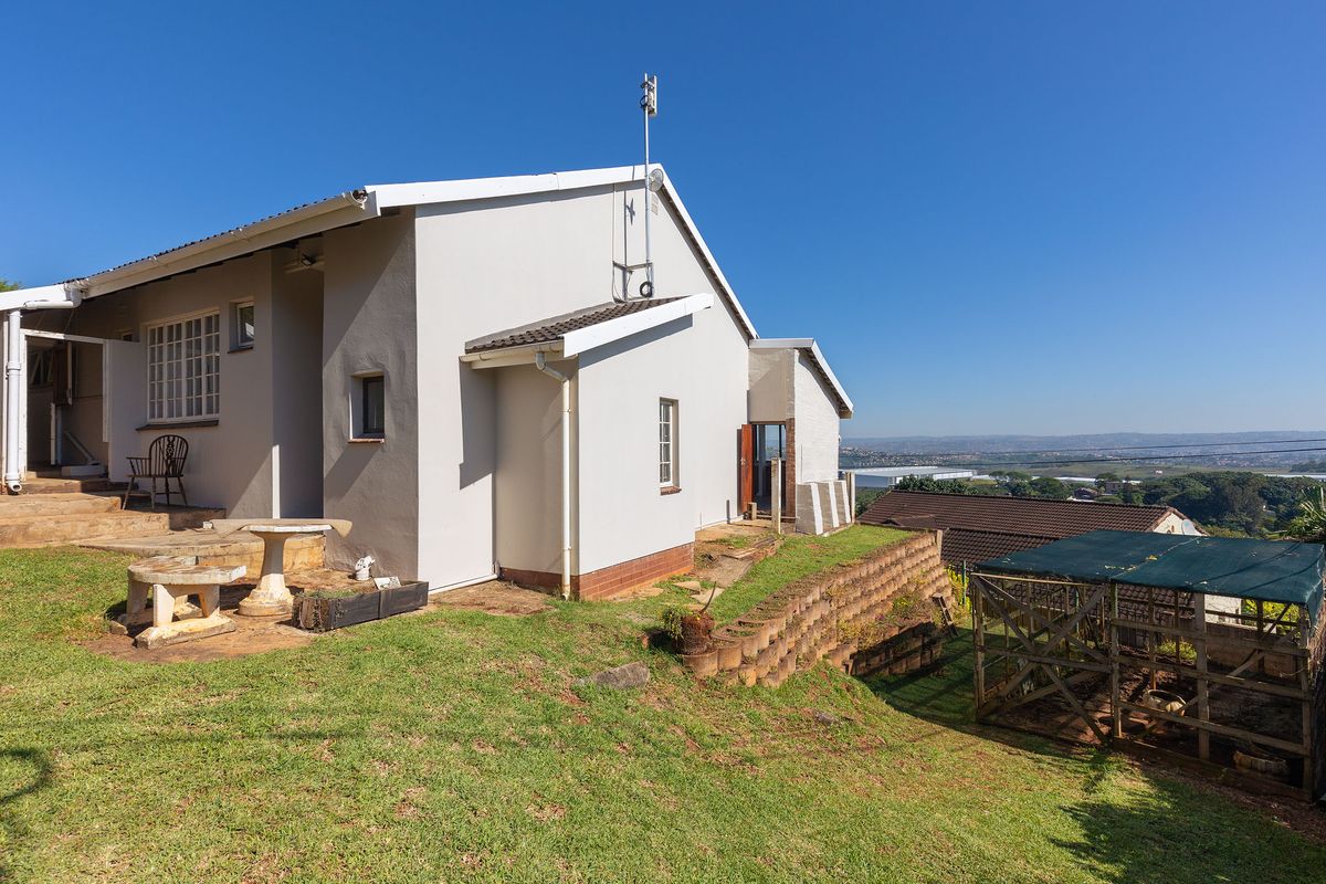 Rear view of the property featuring a concrete patio, retaining wall, and lawn area with distant landscape views.
