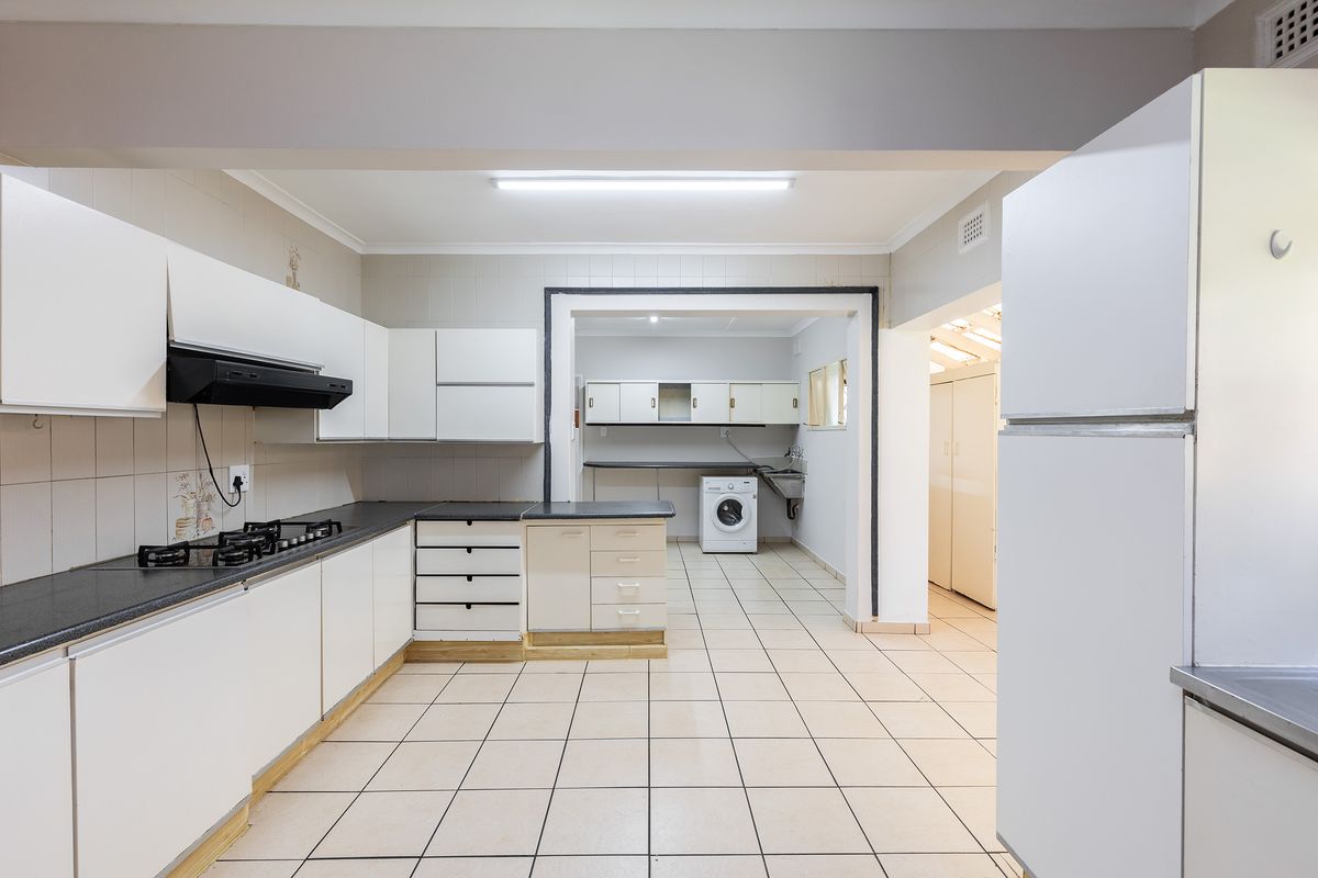 Spacious kitchen featuring white cabinetry, gas hob, extractor fan, and an adjoining laundry area with tiled flooring throughout.