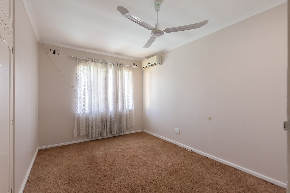 A clean, empty bedroom featuring neutral walls, carpet flooring, a ceiling fan, and a wall-mounted split-system air conditioner.