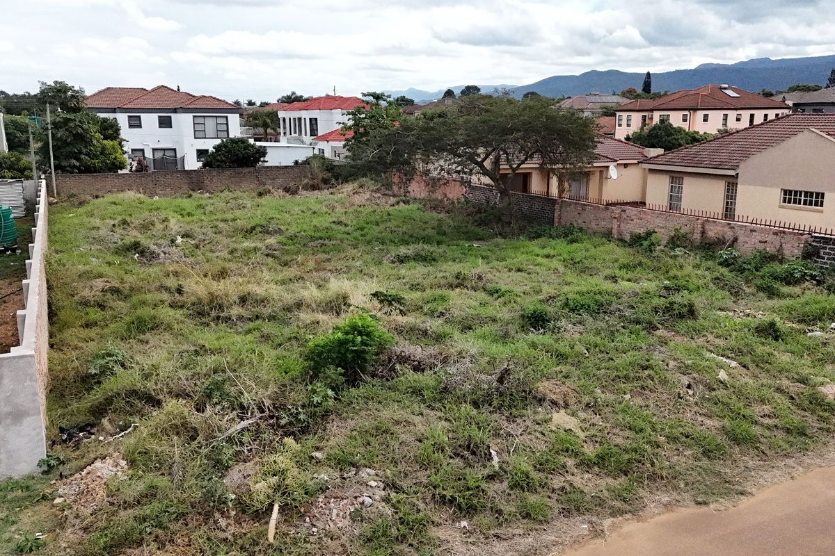 An elevated view of a vacant residential plot featuring perimeter brick boundary walls and established vegetation in a suburban neighborhood setting.