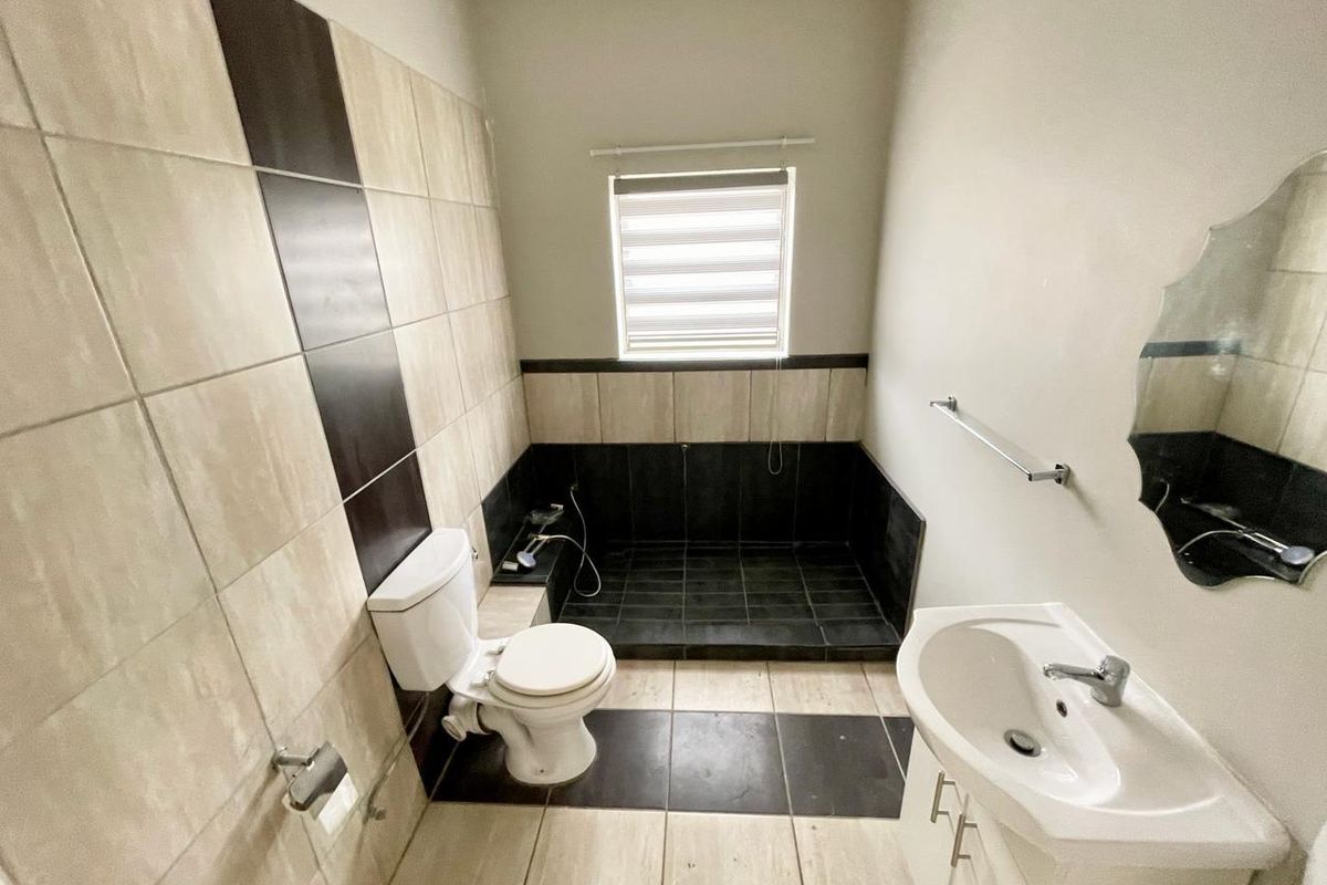 A functional bathroom featuring a walk-in shower area, vanity basin, and toilet with neutral tiled walls and flooring.