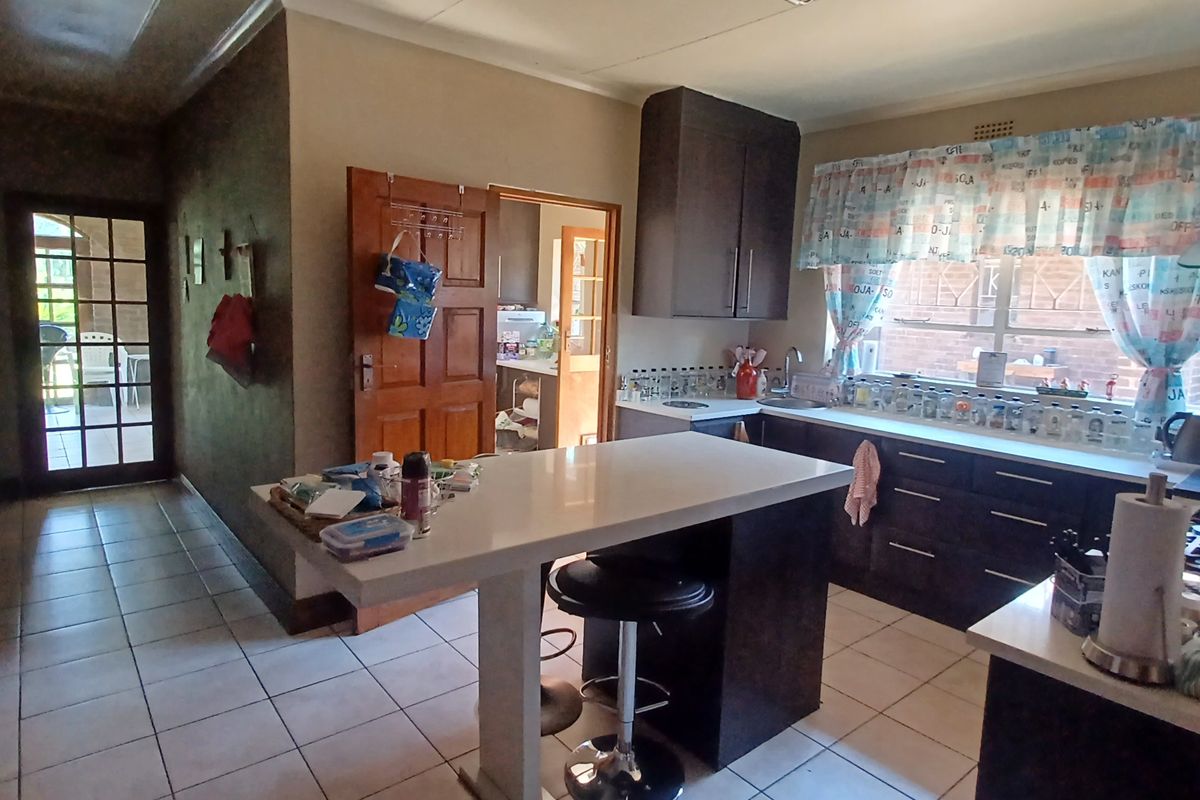 A functional kitchen featuring dark cabinetry, a central island with seating, tiled flooring, and a double sink with a window view.