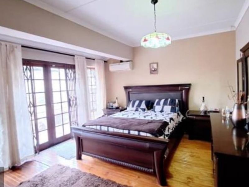 Spacious bedroom featuring hardwood flooring, a wall-mounted air conditioning unit, and direct access to the outdoors through glass-paned french doors with security gates.