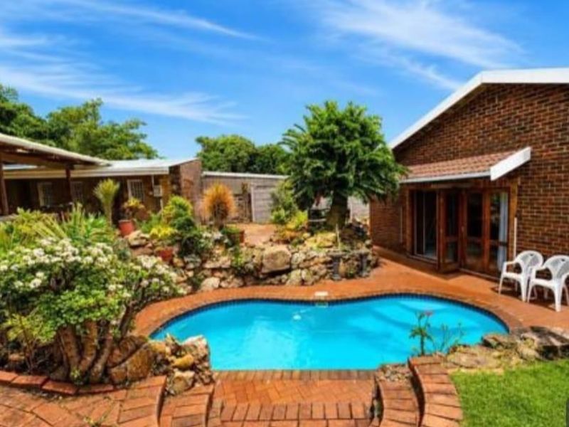 A well-maintained outdoor pool area featuring brick paving, a landscaped rock garden, and direct access to the home via sliding doors.
