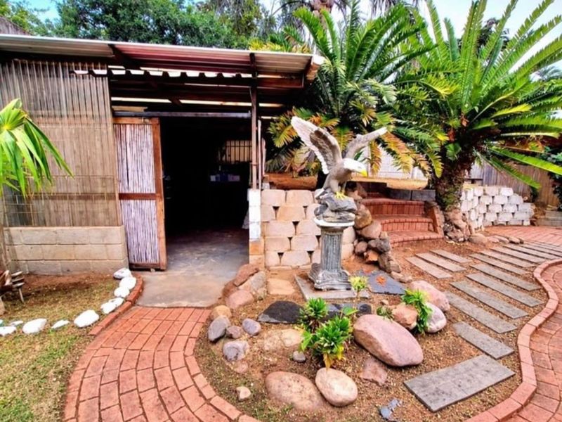 A rear garden area featuring a brick paved pathway, stone landscaping, and a covered outdoor structure with corrugated roofing.