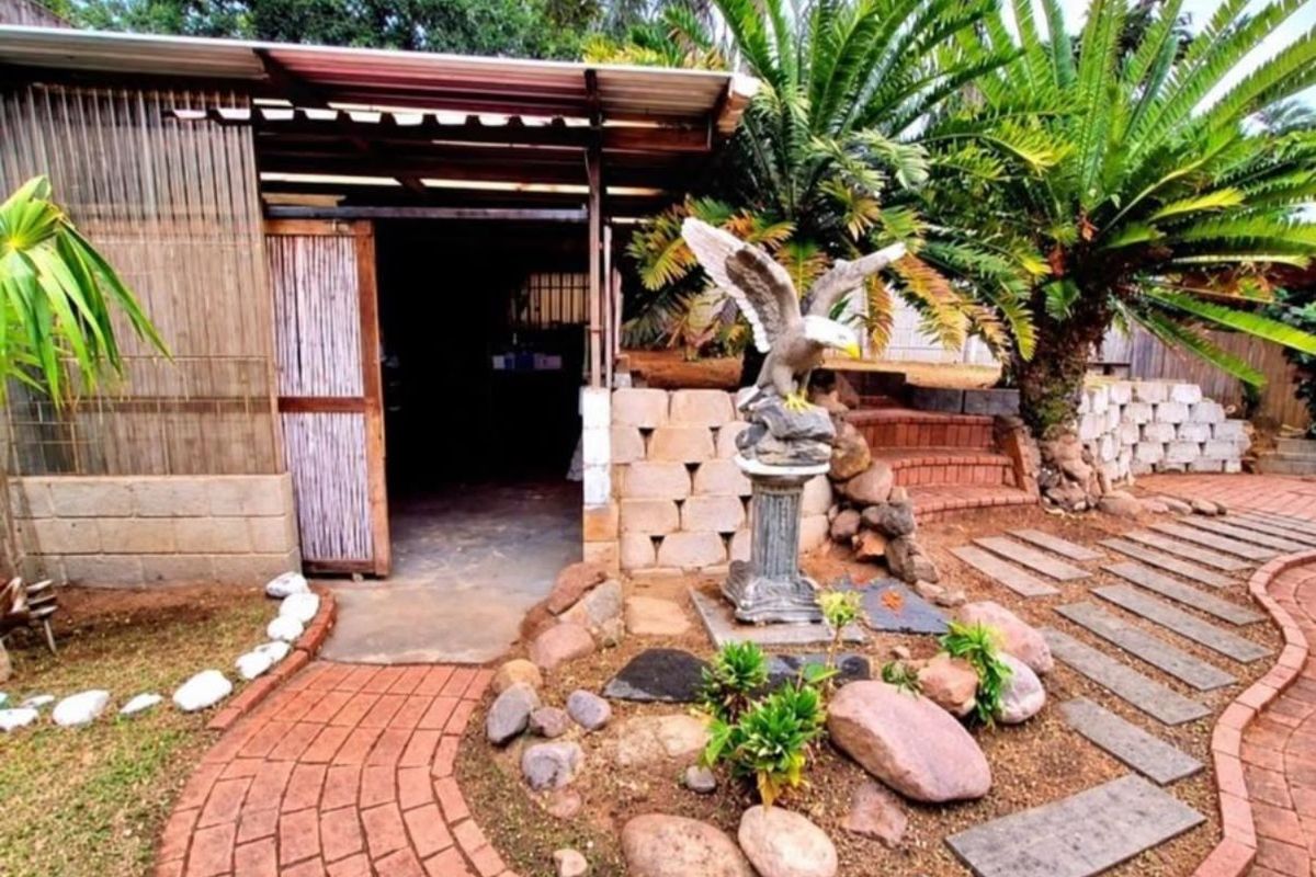 A rear garden area featuring a brick paved pathway, stone landscaping, and a covered outdoor structure with corrugated roofing.
