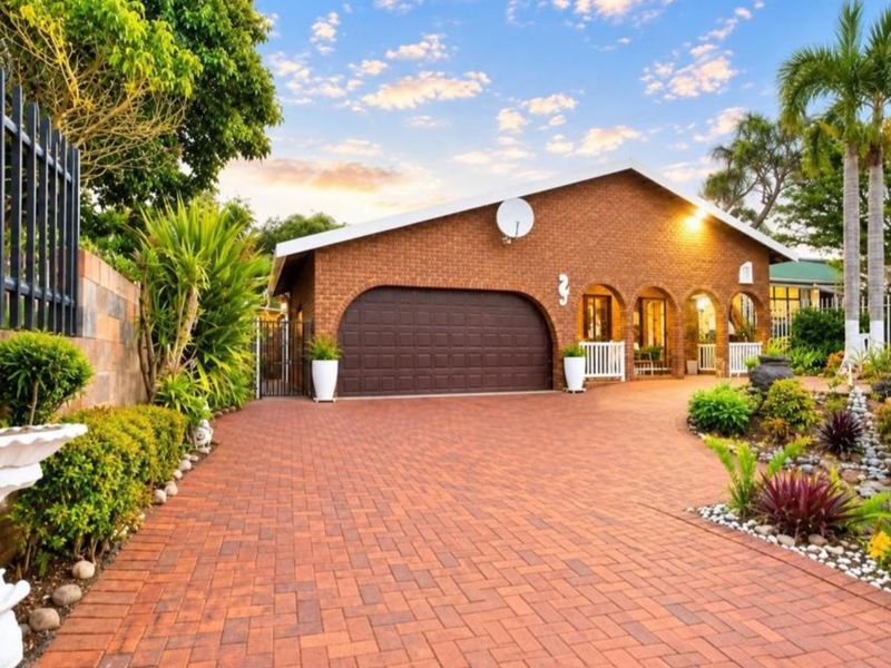 Front view of a well-maintained brick house featuring a paved driveway, double garage, and charming arched entrance with established garden landscaping.
