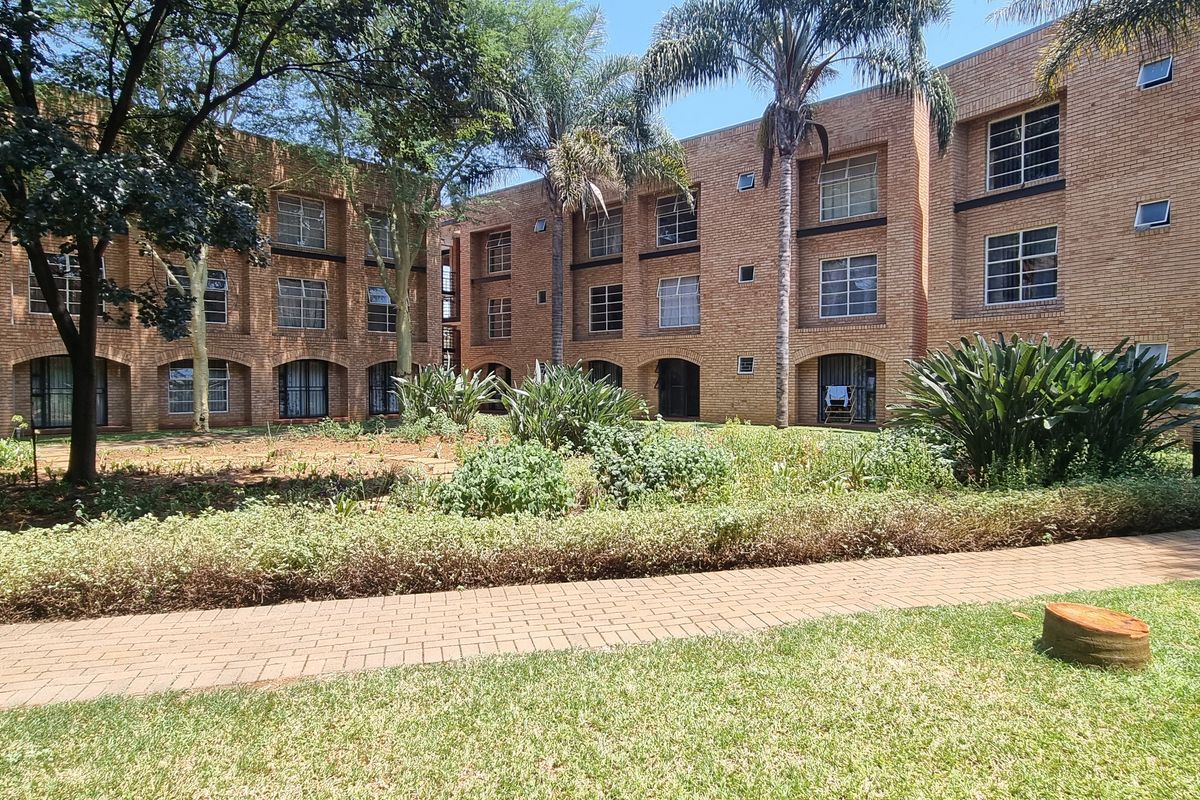 A view of the rear exterior of a multi-story face brick apartment complex featuring a landscaped garden and paved walkway.