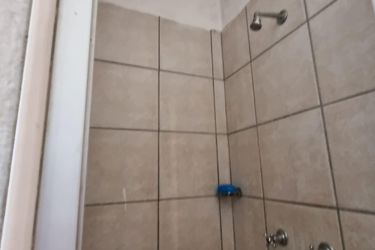 A compact shower enclosure featuring neutral ceramic wall tiles, a standard shower head, and mixer taps, requiring some finishing work to the upper wall area.
