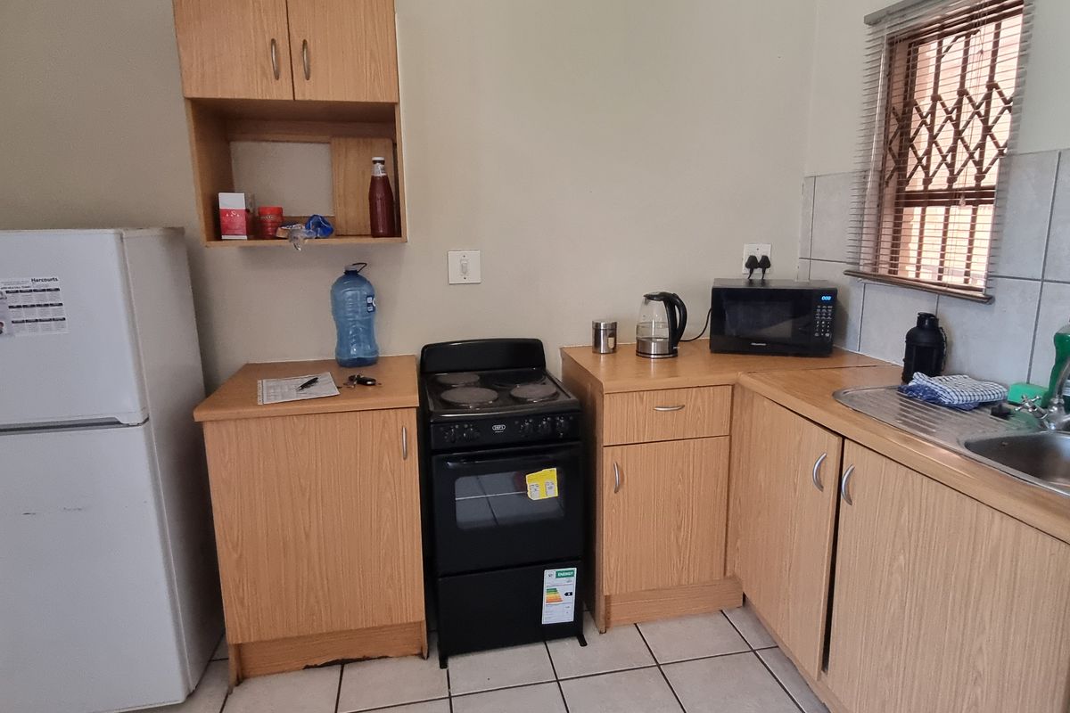 A functional kitchen featuring laminate cabinetry, a stainless steel sink, tiled backsplash, and ceramic flooring, providing a practical and compact cooking space.