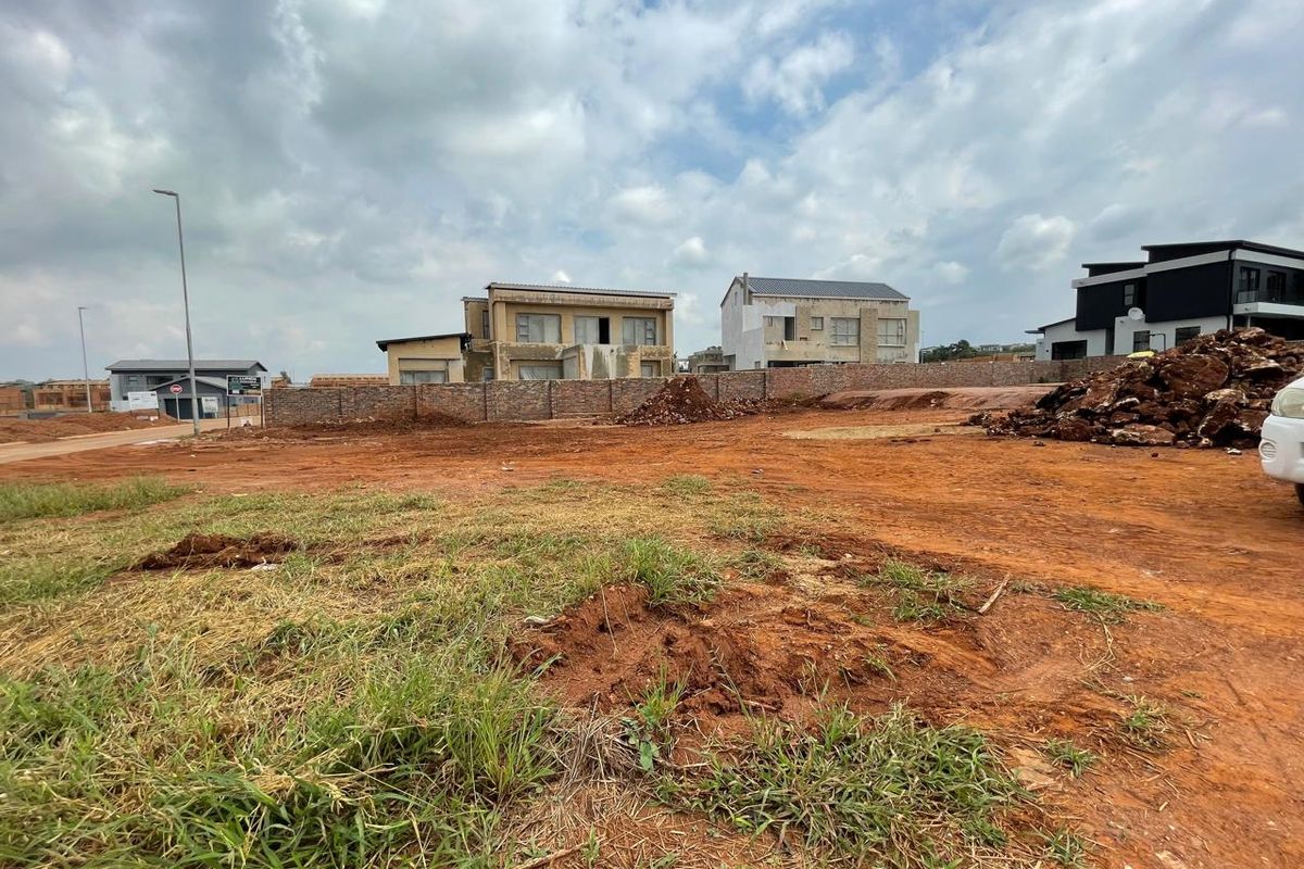 A vacant plot of land featuring a brick boundary wall, situated in a developing residential estate with surrounding modern homes.