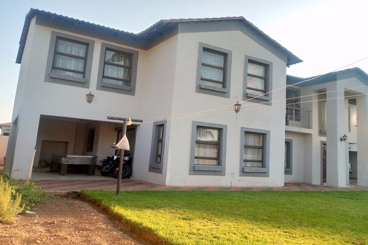A two-story residential property featuring a paved driveway, covered patio area, balcony, and a rear garden space.
