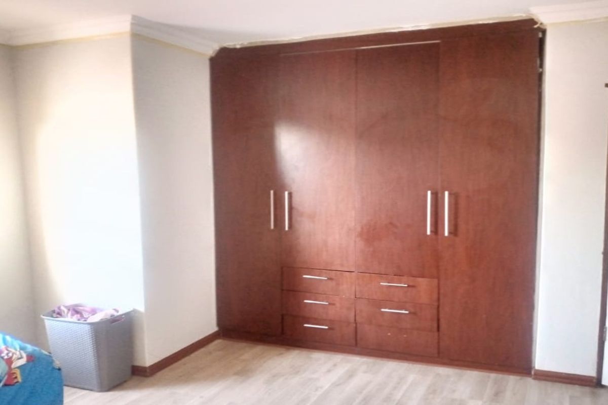 A bedroom featuring built-in wooden cupboards, laminate flooring, and coving. The space offers functional storage and neutral finishes.
