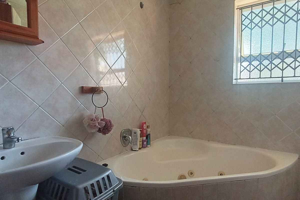 Bathroom featuring a corner bathtub, pedestal basin, and tiled walls. The space requires maintenance, specifically addressing cracked tiling above the window.