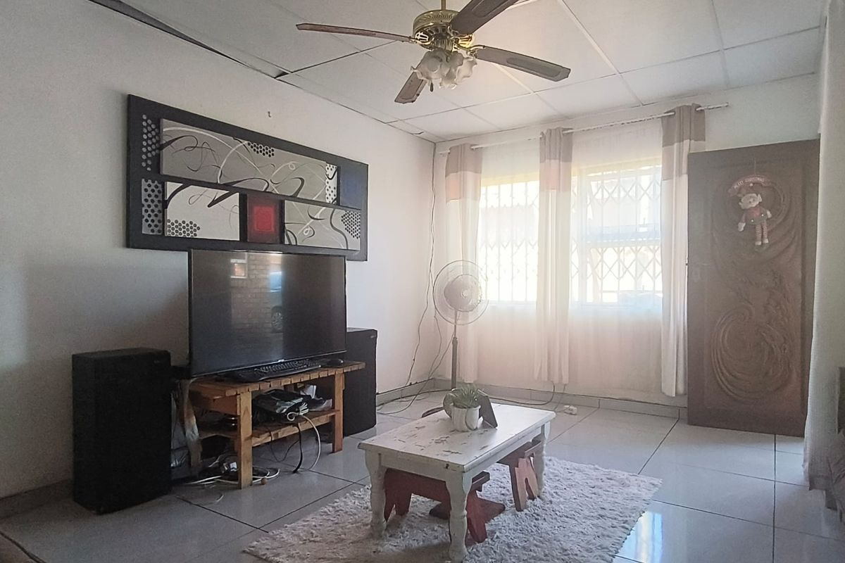 A living room featuring tiled flooring, a ceiling fan, and a drop ceiling, with security gates on the windows.