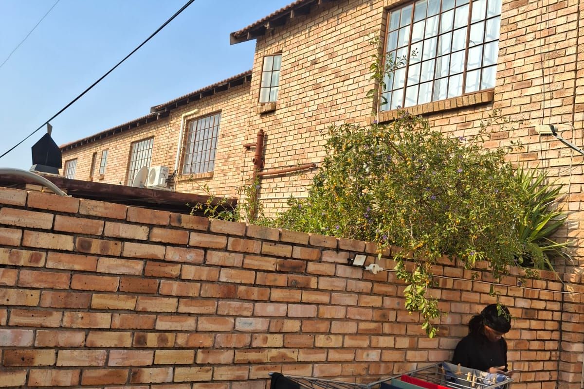 Exterior view of a multi-story brick apartment building featuring large grid-style windows and a private brick-walled courtyard area.