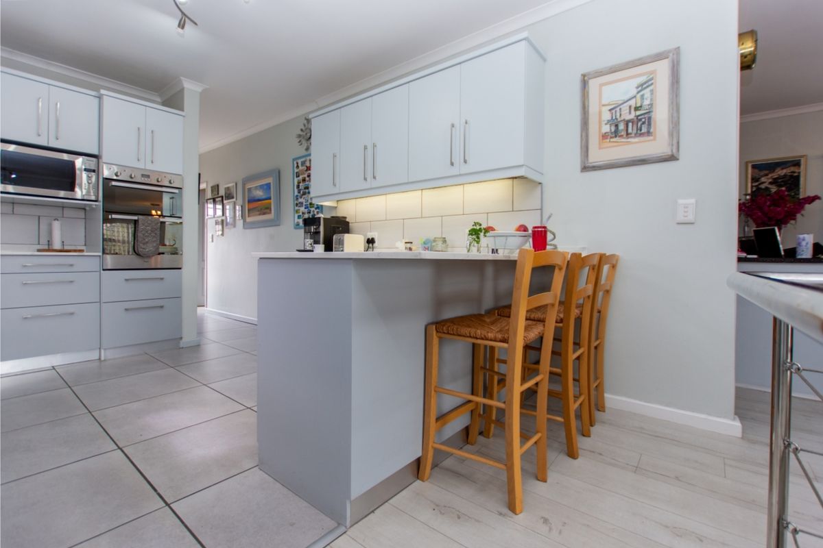 A well-maintained kitchen featuring light-toned cabinetry, built-in appliances, a central island with breakfast bar seating, and a combination of tiled and laminate flooring.