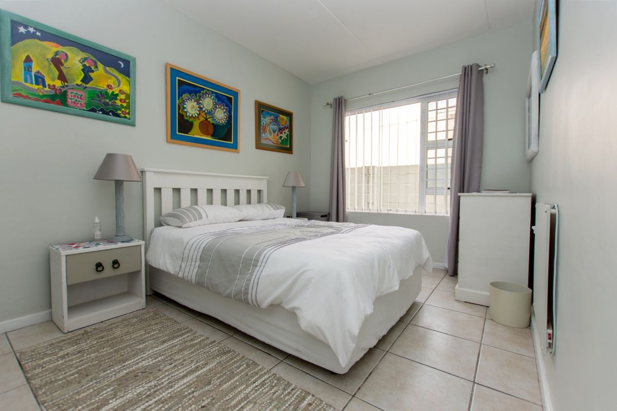 A well-maintained bedroom featuring neutral tiled flooring, light-colored walls, and a window fitted with security bars and vertical blinds.