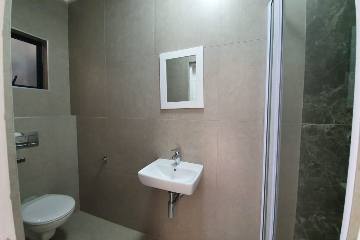 Modern bathroom featuring large-format neutral wall tiles, a wall-mounted basin with chrome mixer, concealed cistern toilet, and a glass-enclosed shower.