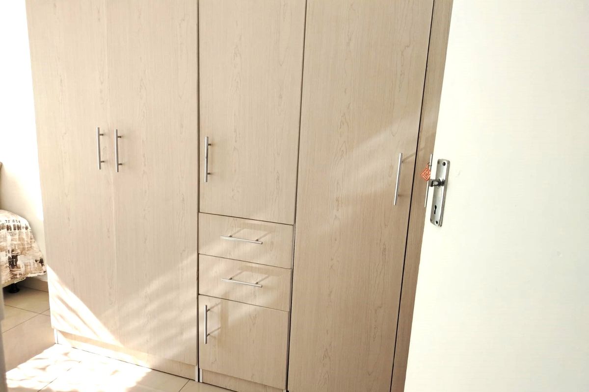 A bedroom featuring light wood-grain built-in cupboards with integrated drawers and modern metal handles.