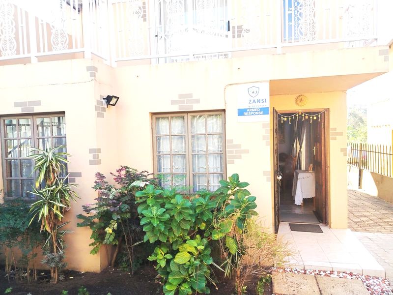 A view of the property entrance featuring a paved walkway, security signage, and a balcony above the ground floor access point.