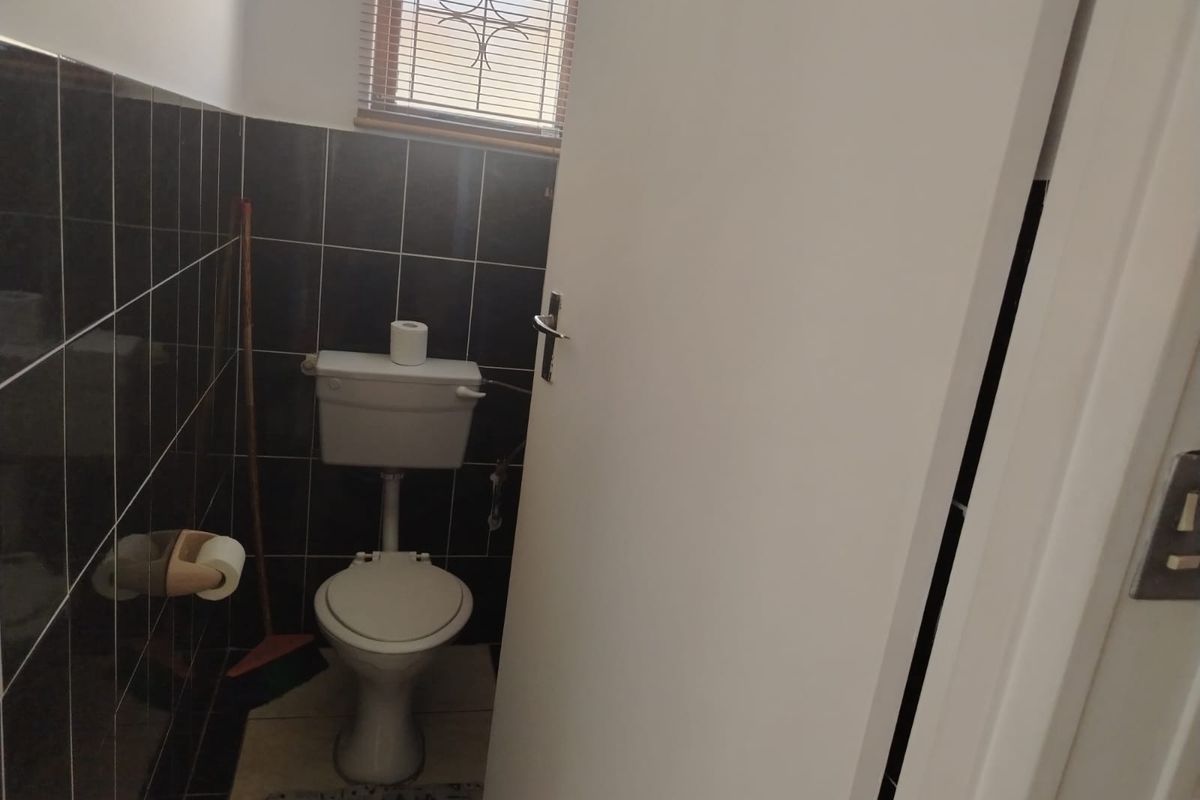 A compact bathroom featuring dark wall tiling, a standard white toilet, and a window with fitted blinds.