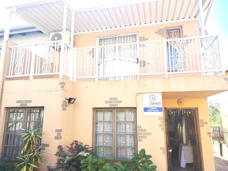 Two-story residential facade featuring a covered upper-level balcony with decorative metal railings, ground-floor entrance, and security-fitted windows.