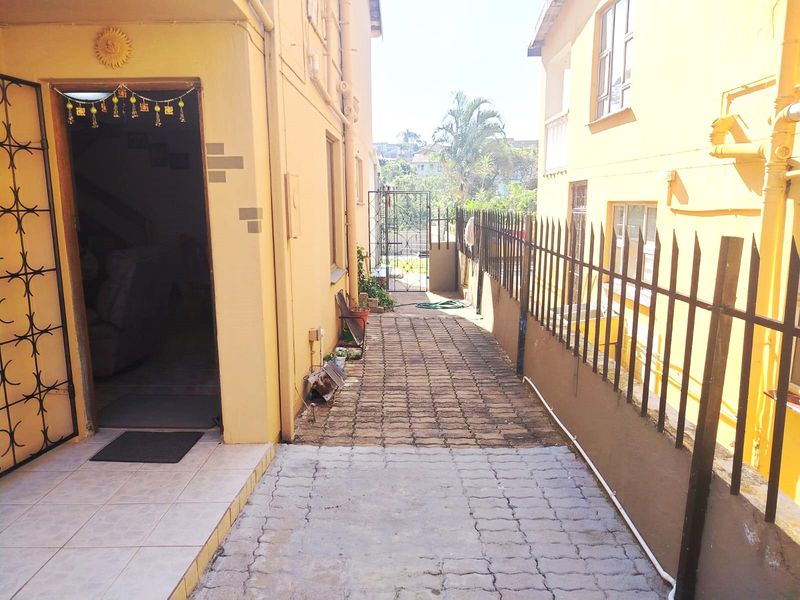 A side walkway featuring paved flooring, metal security fencing, and access to the main building entrance.