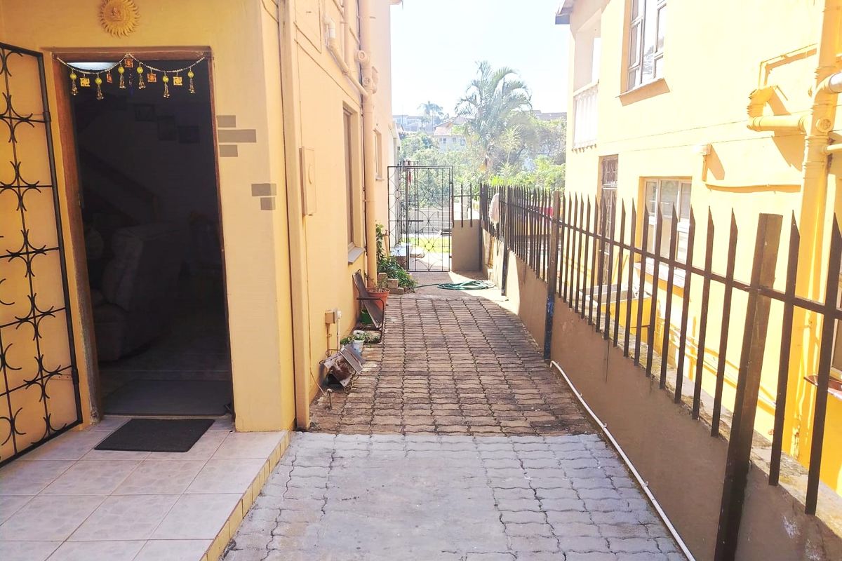 A side walkway featuring paved flooring, metal security fencing, and access to the main building entrance.
