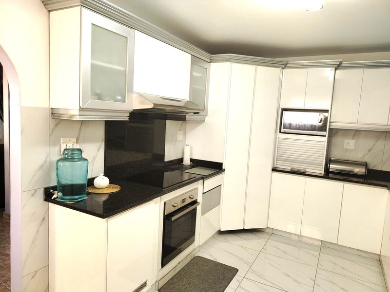 Modern kitchen featuring white high-gloss cabinetry, black granite countertops, integrated oven, electric hob, and marble-look floor tiles.