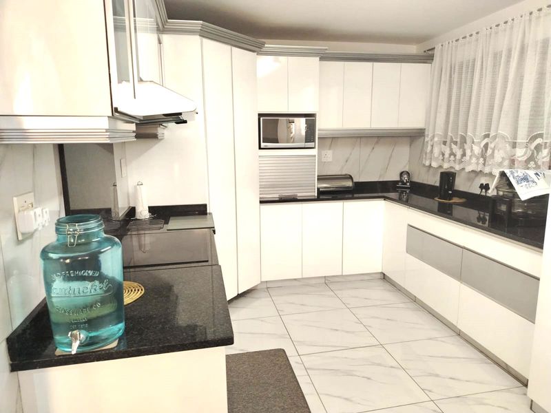 Modern kitchen featuring white cabinetry, contrasting black granite countertops, built-in microwave, and tiled flooring.