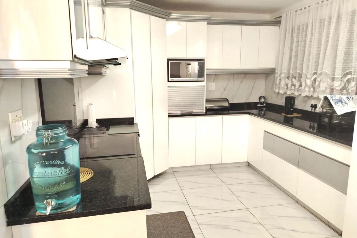 Modern kitchen featuring white cabinetry, contrasting black granite countertops, built-in microwave, and tiled flooring.