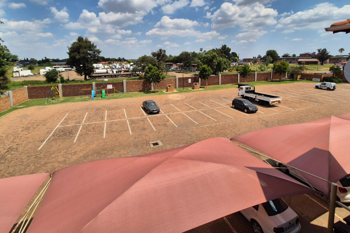 Elevated view of a paved communal parking area featuring shade cloth carports and a brick boundary wall.