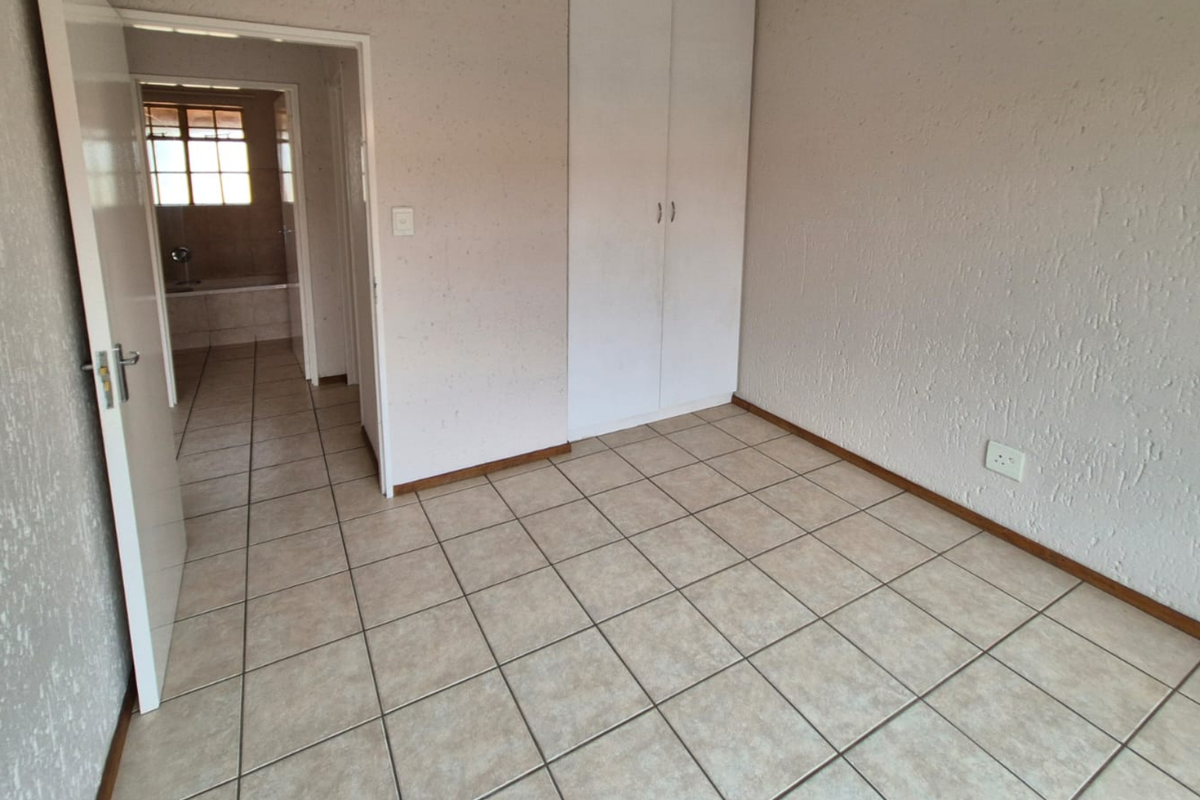 An empty bedroom featuring tiled flooring, textured walls, and a built-in wardrobe, with an adjacent view into a bathroom area.