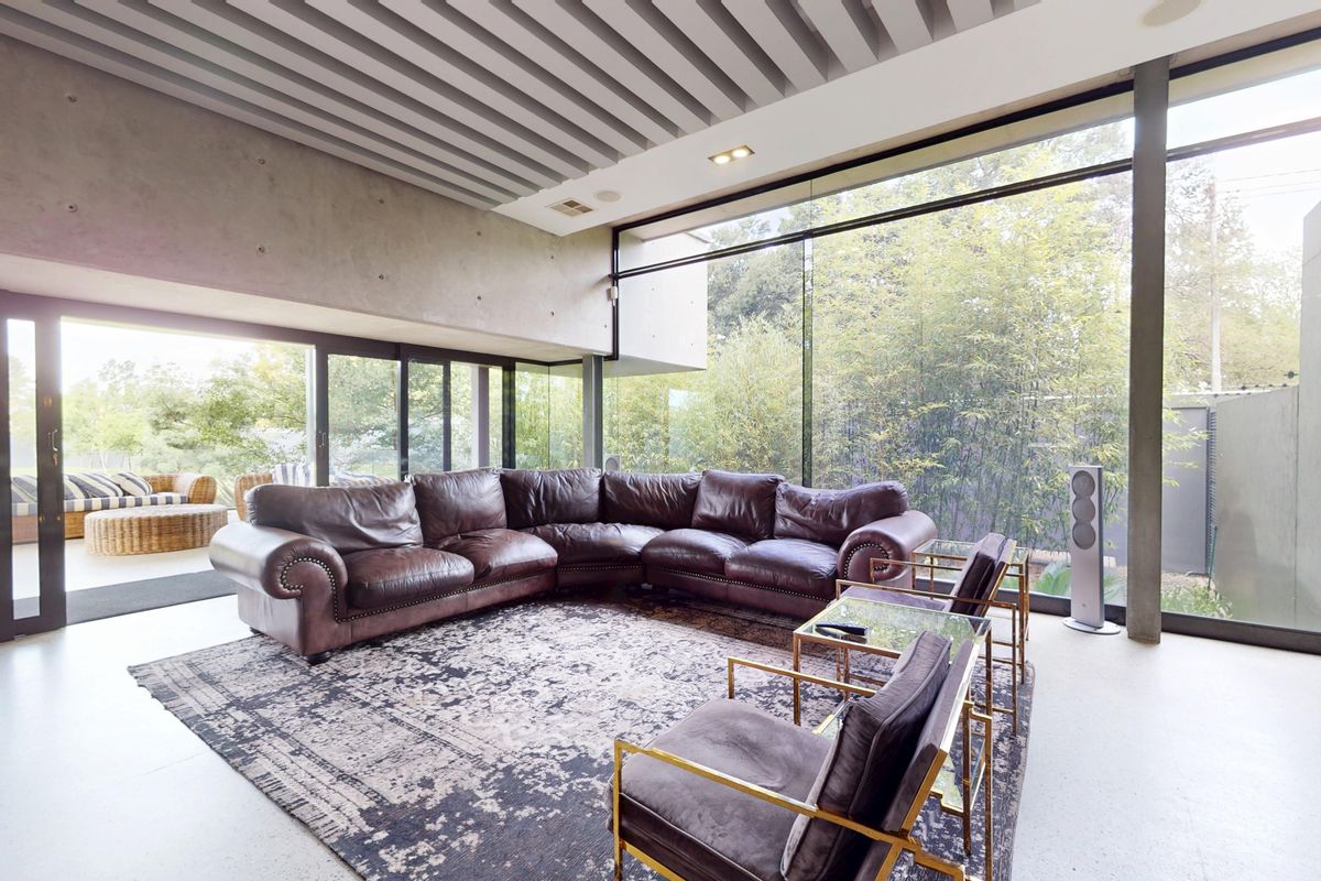 Modern living room featuring expansive floor-to-ceiling glass walls, exposed concrete finishes, and a unique slatted ceiling, seamlessly connecting to the outdoor garden area.
