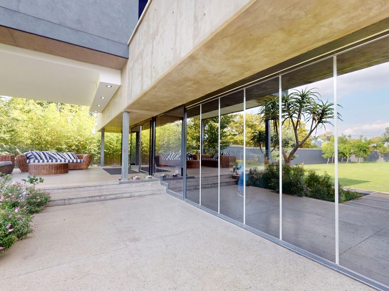A modern covered patio featuring polished concrete flooring, recessed lighting, and expansive frameless glass sliding doors that open onto a landscaped garden.