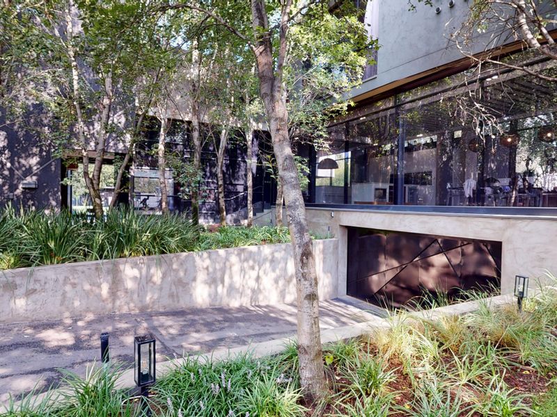 Modern architectural exterior featuring a large glass facade, landscaped garden, and a discreet underground garage entrance with concrete retaining walls.