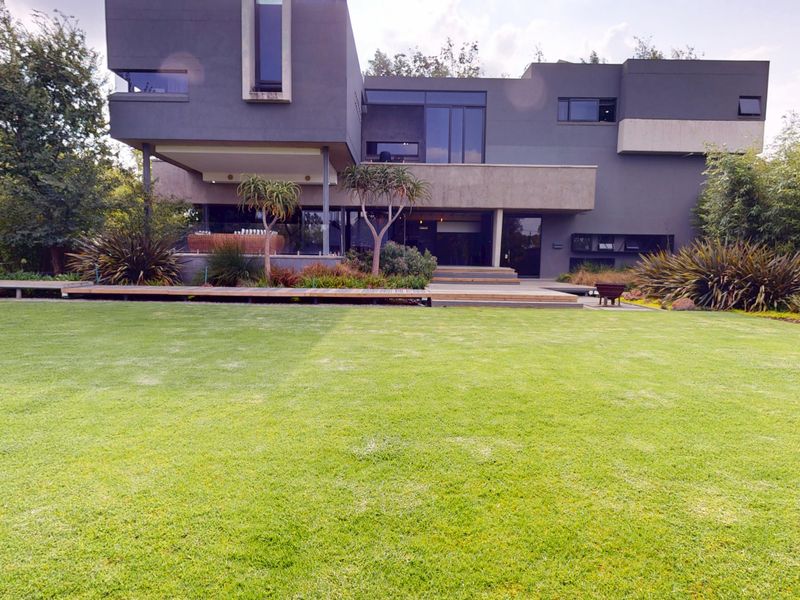 A modern architectural rear elevation featuring a spacious manicured lawn, timber decking, and a covered patio area with large glass windows.