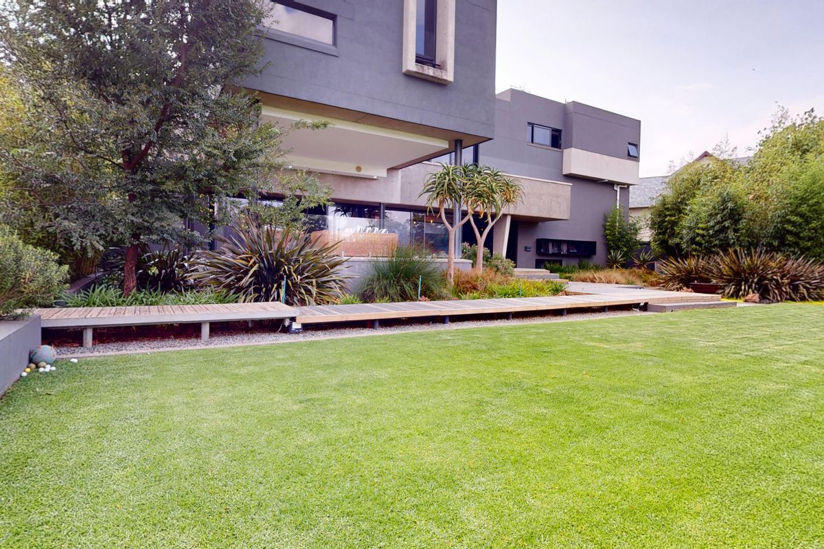 A well-maintained rear garden featuring a modern architectural facade, manicured lawn, and a timber deck walkway.