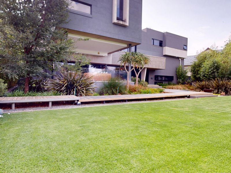 A well-maintained rear garden featuring a modern architectural facade, manicured lawn, and a timber deck walkway.