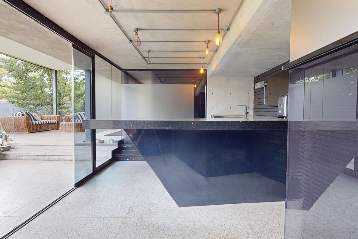 Modern kitchen featuring an industrial aesthetic with exposed concrete ceilings, a large stone island, and seamless indoor-outdoor flow through expansive sliding glass doors.