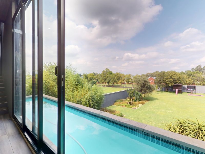 Elevated view of a modern swimming pool overlooking a spacious landscaped garden and lawn area, accessed via large sliding glass doors.