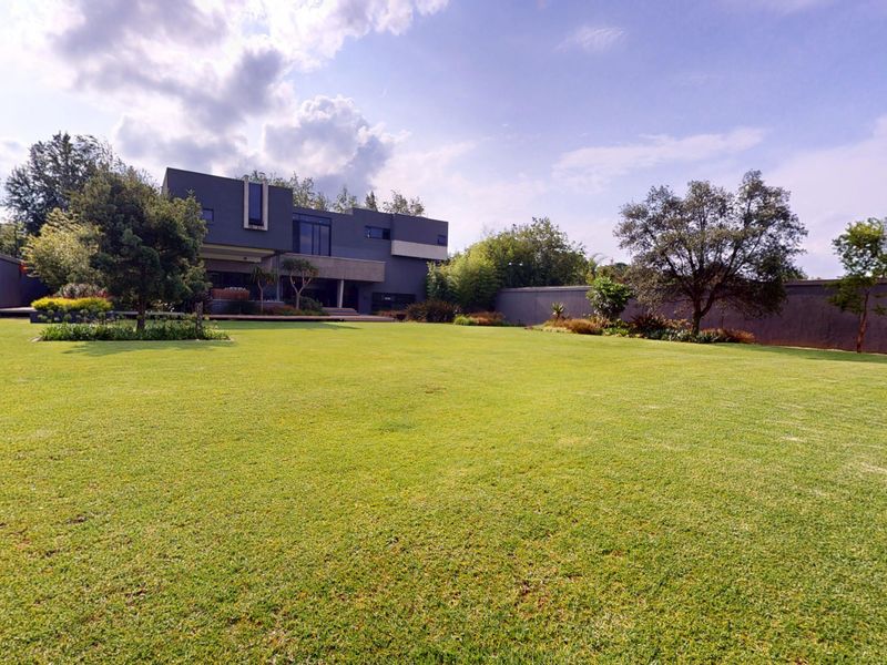 A spacious rear garden featuring a well-maintained lawn, mature trees, and high boundary walls, providing a private outdoor setting for the modern residence.